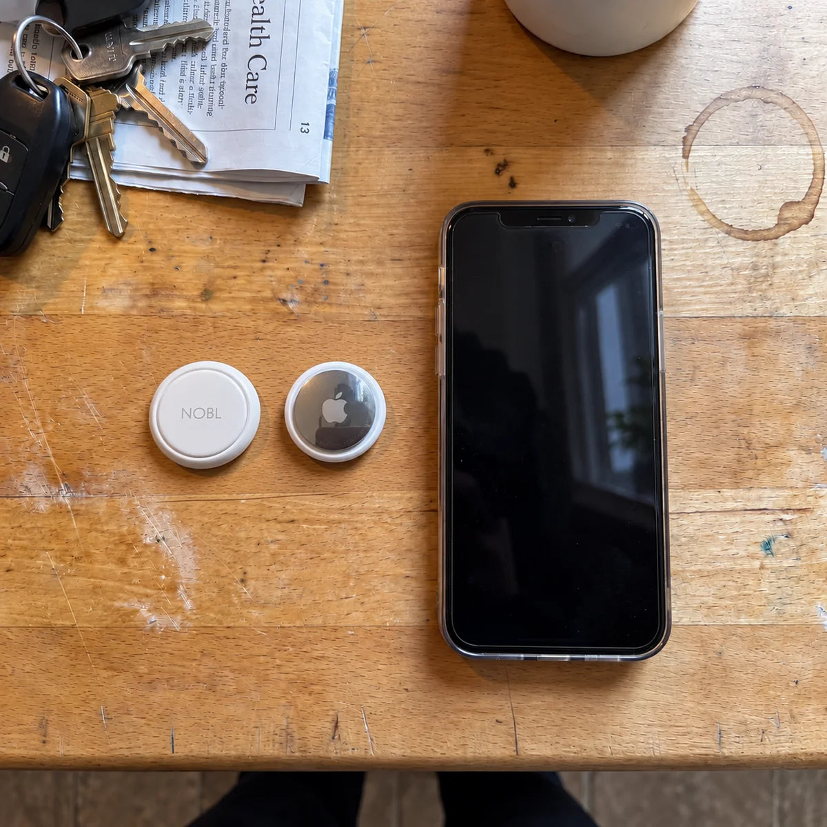 NOBL Air and AirTag beside a phone on a wooden table