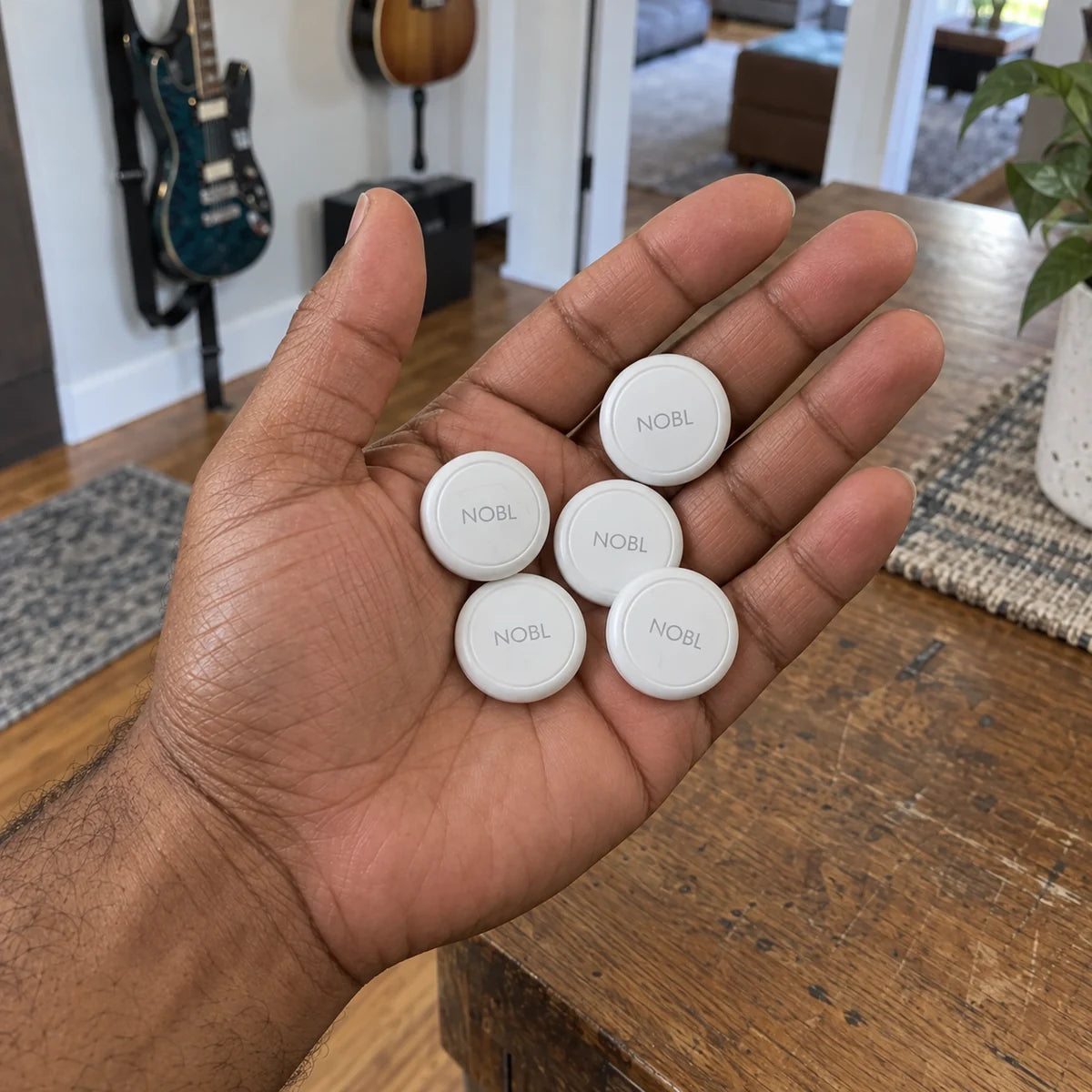 Five NOBL Air trackers in a man's palm above a wooden table